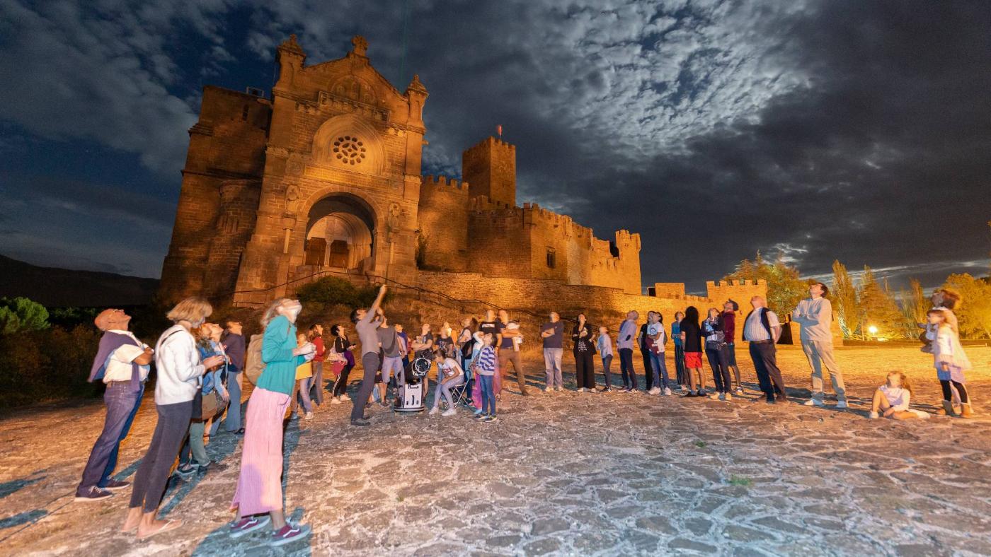 Iluntzean Castillo de Javierren aurrean izarrak behatzen ari diren pertsona taldea